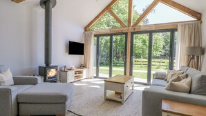 A spacious living room with a high ceiling, a fireplace, a television, and large windows offering a view of the outdoors. - Robins Nest (Fareham)