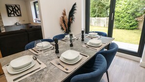 A dining table set with plates, cutlery, and glasses, surrounded by blue chairs, with a view of greenery outside. - Millhouses Hideaway (Sheffield)