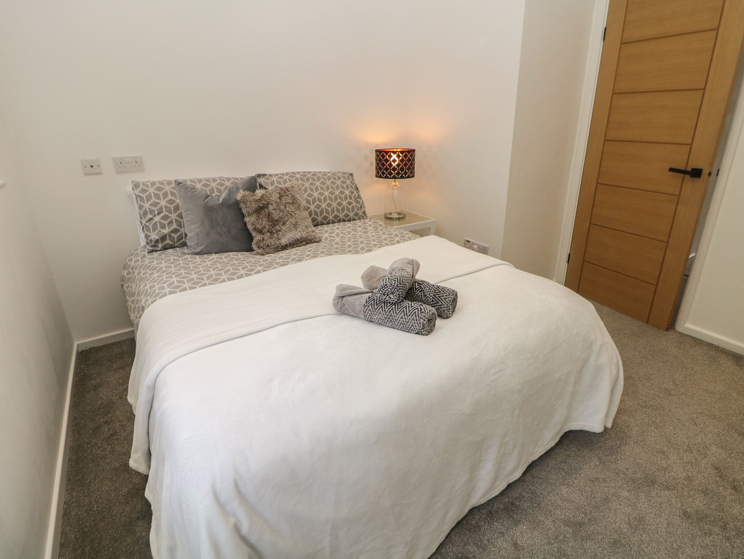 A neatly made bed with a white duvet and two patterned towels, a bedside lamp, and a patterned headboard.