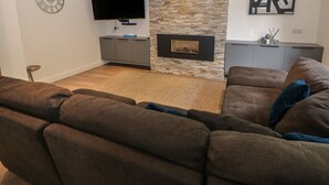 A modern living room with a stone fireplace, a flat-screen TV, and a grey cabinet. - Millhouses Hideaway (Sheffield)