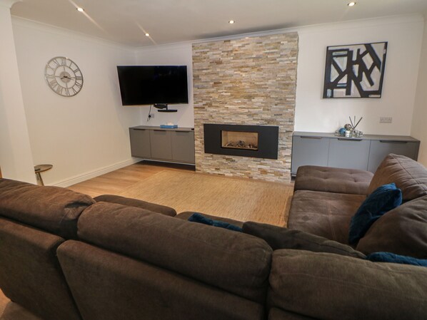 A modern living room with a stone fireplace, a flat-screen TV, and a grey cabinet. - Millhouses Hideaway (Sheffield)