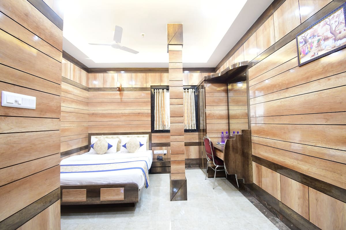 Ein modernes Hotelzimmer mit Wandverkleidung aus Holz, einem Bett mit blauen Akzenten, einem Schreibtisch und einem Deckenventilator.