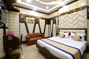 A hotel room with a large bed, a brown leather sofa, a wooden vanity, and a mirror. - Hotel Margaret (Kolkata)