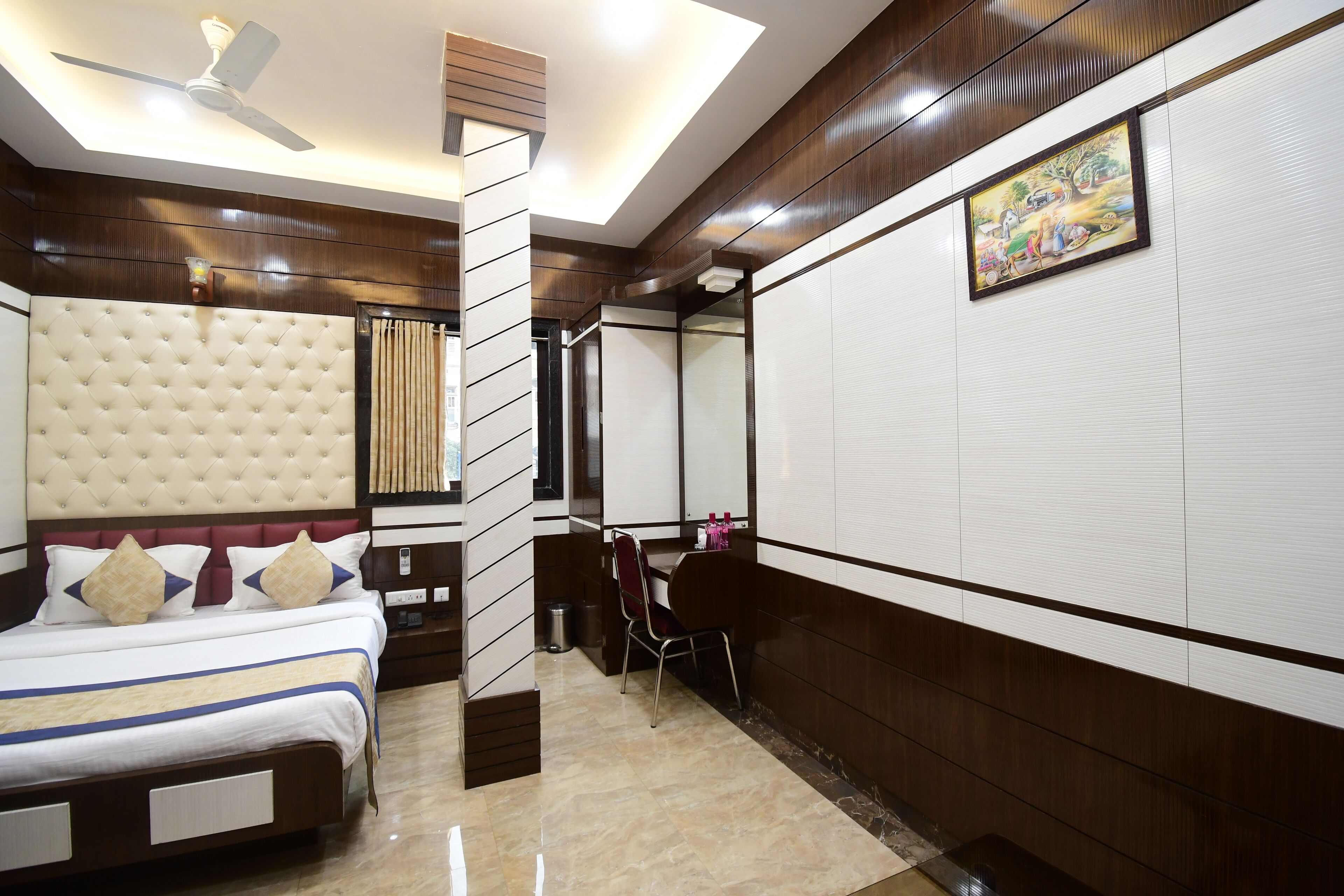 Habitación de hotel con una cama grande, un ventilador de techo, un cuadro en la pared y una pequeña mesa con sillas.