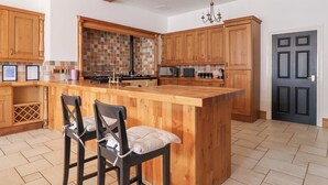 Une cuisine moderne avec des meubles en bois, un grand îlot central doté de tabourets, un pare-feu en carrelage et un lustre.