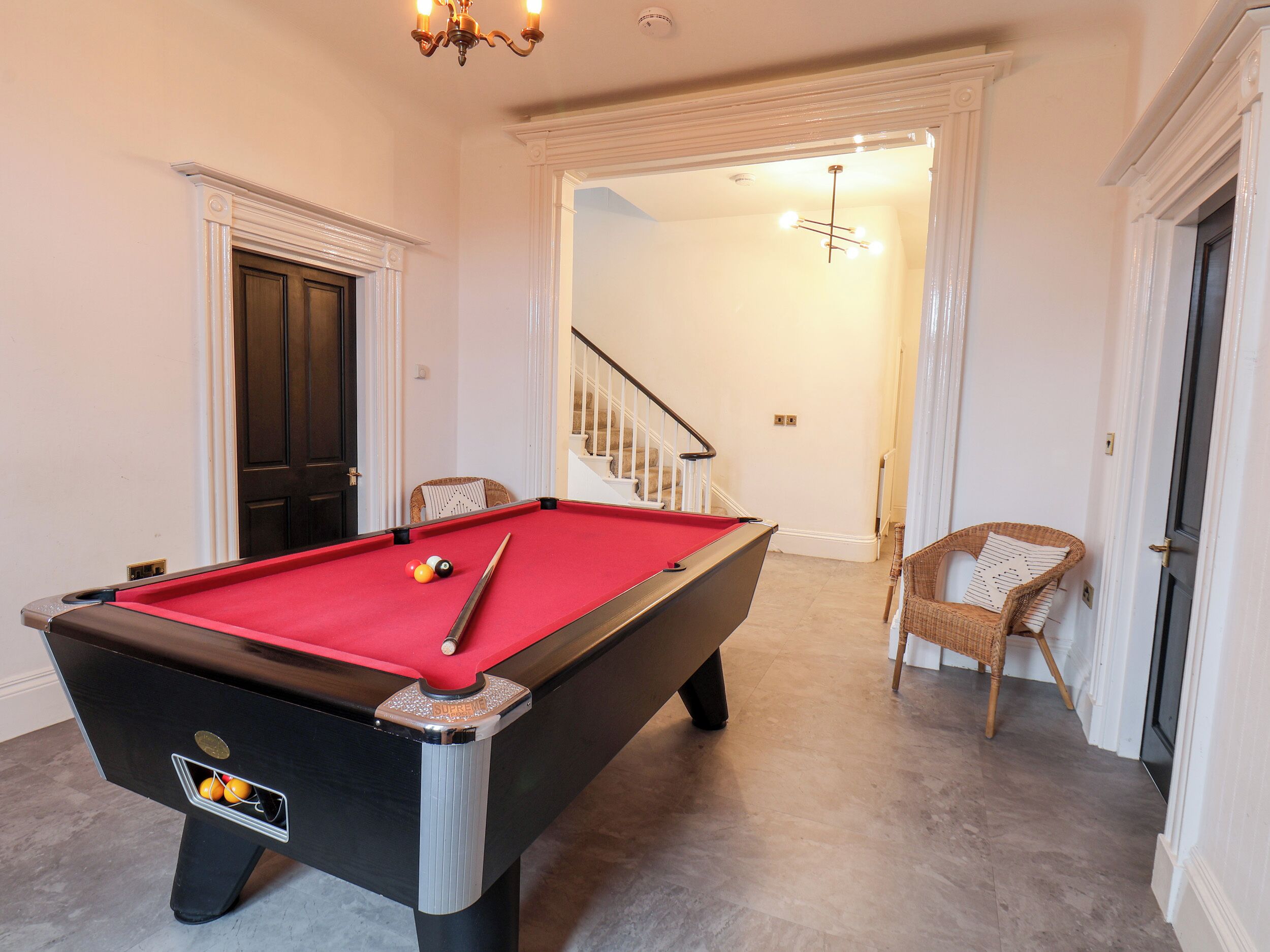 A pool table with balls, a chair, and a staircase leading to another room.