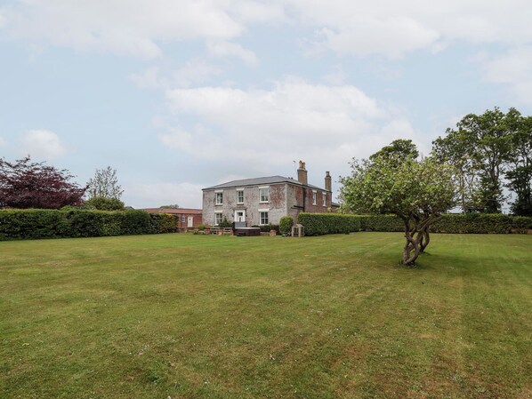 A large, two-story house with a well-maintained lawn and a hedge in the foreground.