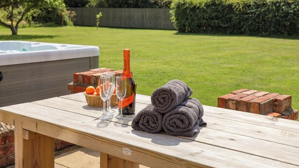 Une table de pique-nique en bois, un jacuzzi, une bouteille de champagne, des verres et des serviettes.