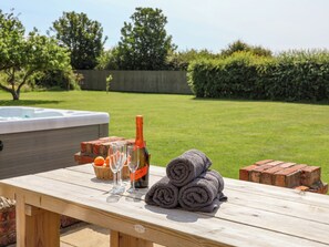 A wooden picnic table with a hot tub, a bottle of champagne, glasses, and towels.