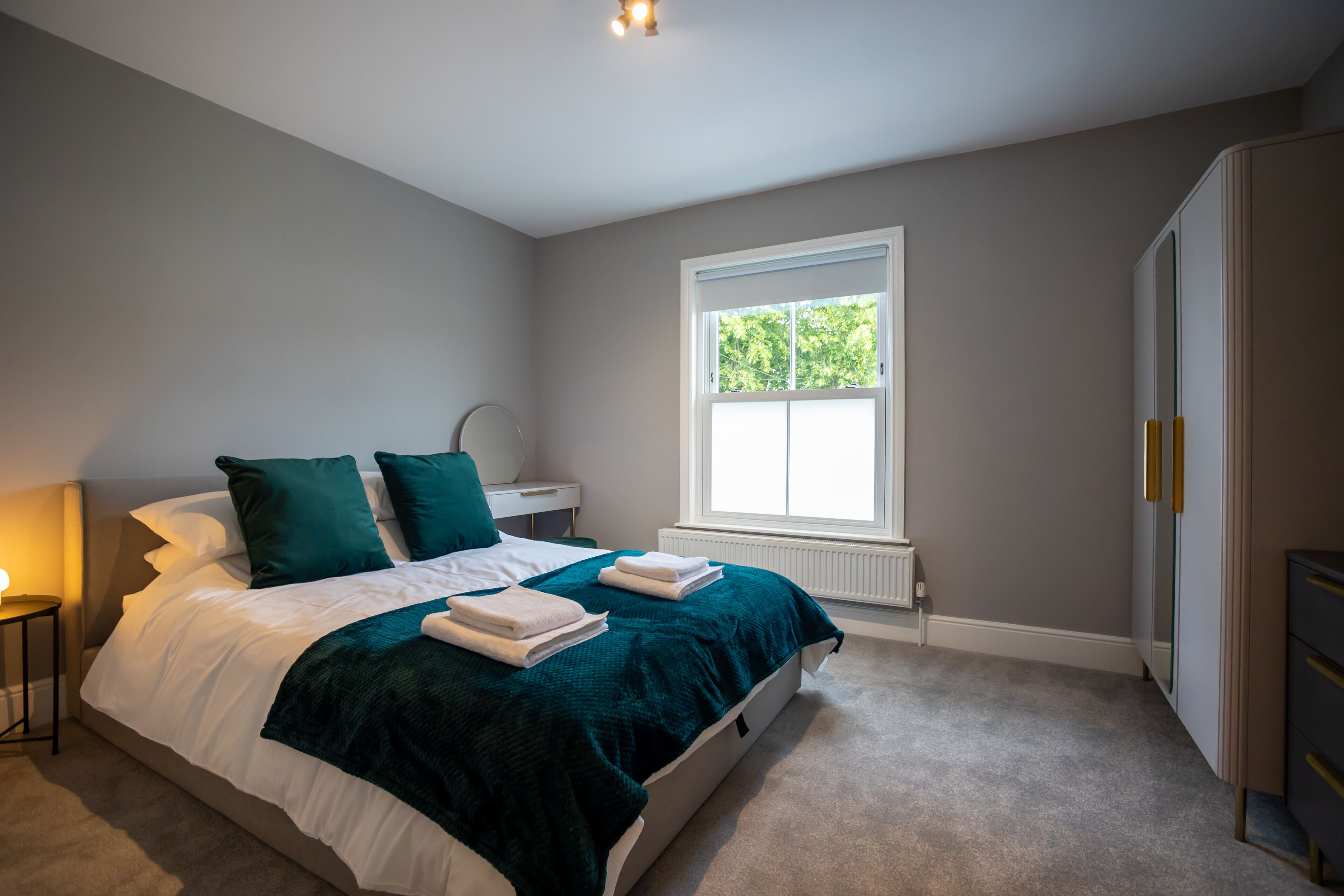 A bedroom with a bed, a nightstand, a window, and a wardrobe.