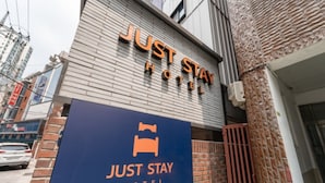 Une enseigne d’hôtel avec l’inscription « JUST STAY HOTEL » et une autre enseigne bleue avec un symbole de lit et l’inscription « JUST STAY HOTEL ».