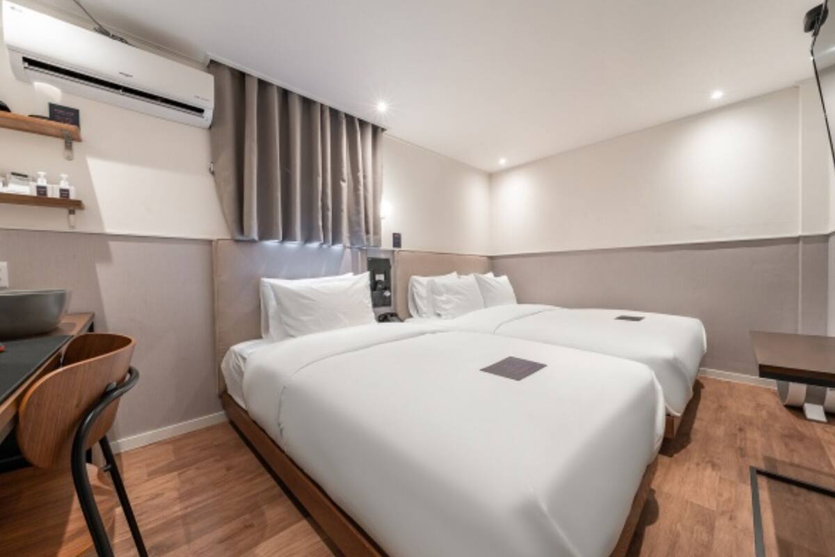 Une chambre d’hôtel avec deux lits, un bureau, une chaise et un appareil de climatisation.