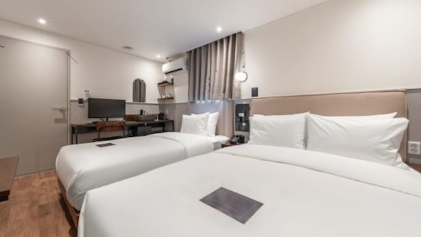 Une chambre d’hôtel avec deux lits, un bureau, une chaise, une télévision et une fenêtre avec des rideaux.