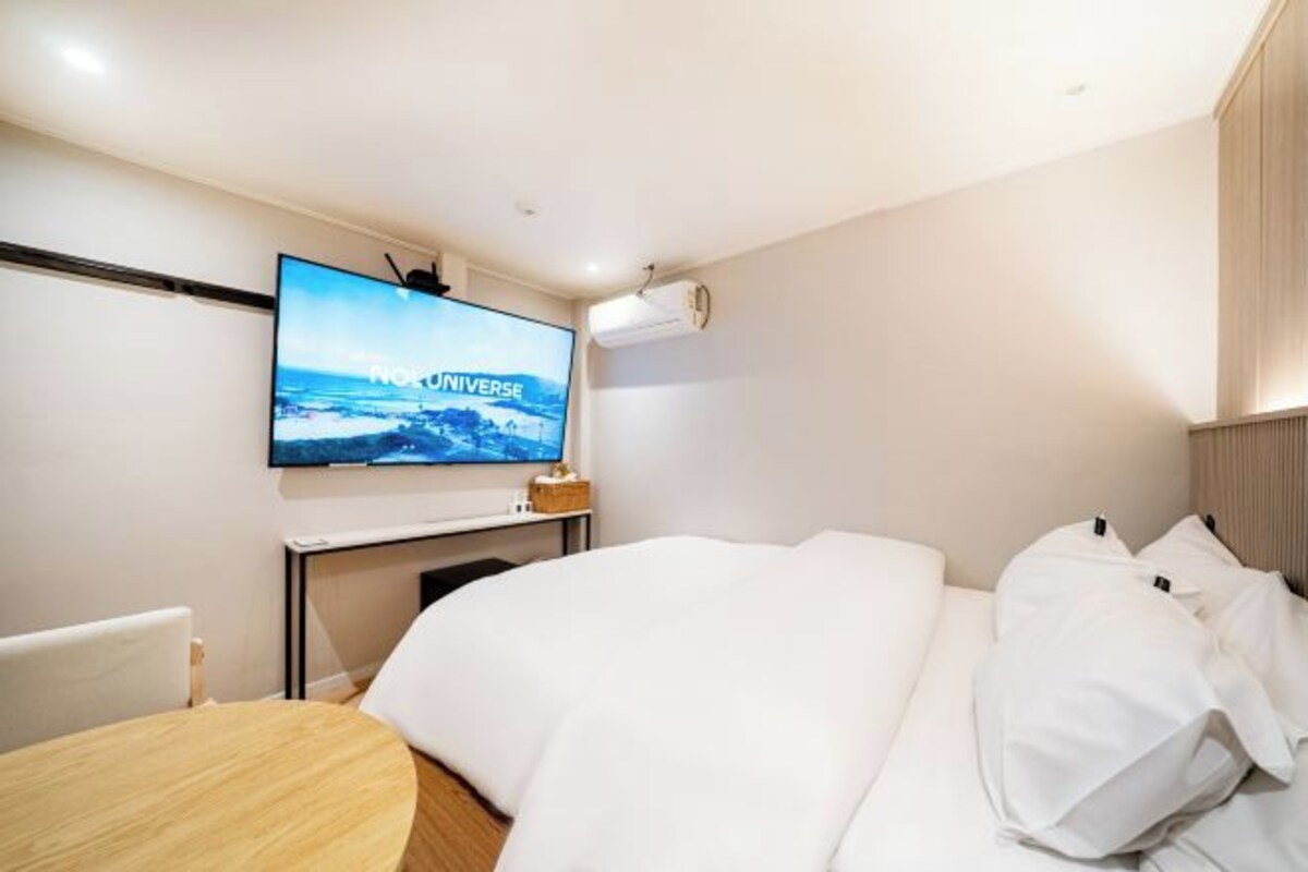 Una habitación de hotel con una cama, un televisor montado en la pared y una mesita.