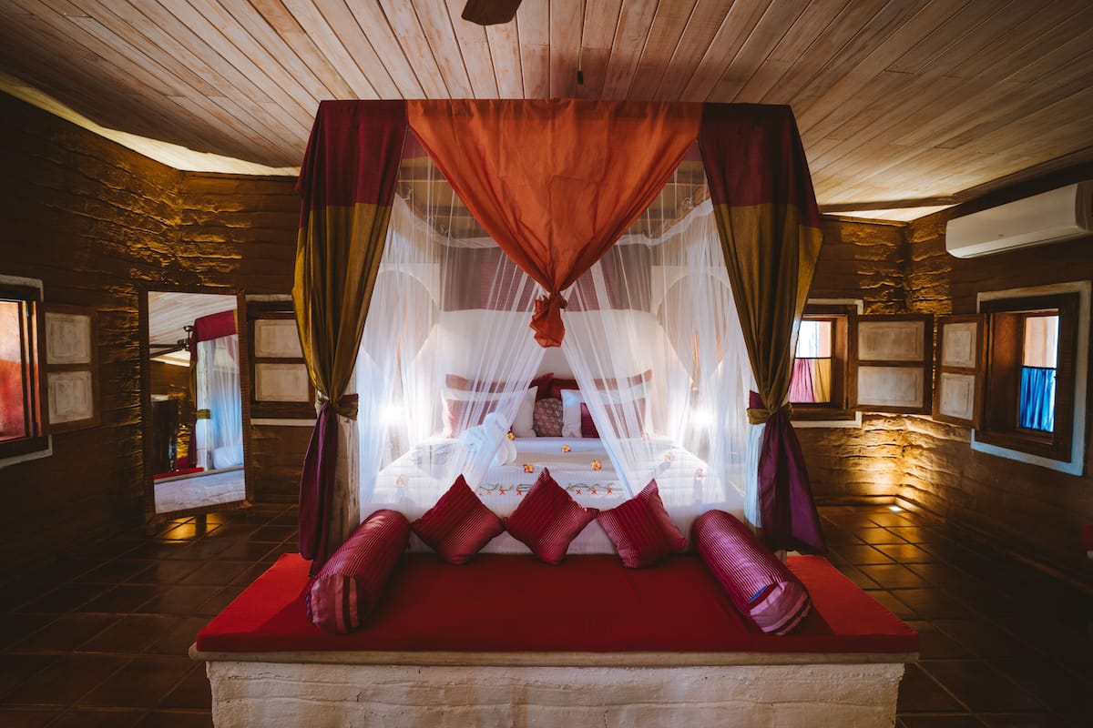 Ein Zimmer mit einem Bett unter einem Baldachin, Steinwänden und einer Holzbalkendecke.