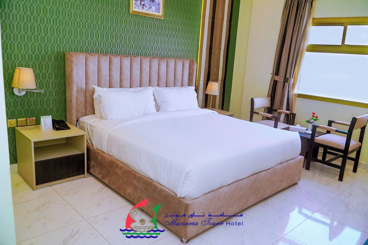 A hotel room with a large bed, a nightstand, a desk with a chair, and a window with curtains.
