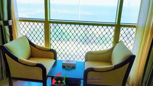 A room with two chairs and a table, a window with a view of the sea, and a logo for Manana Suites Hotel. - Capital O 126 Manama Tower Hotel (Manama)