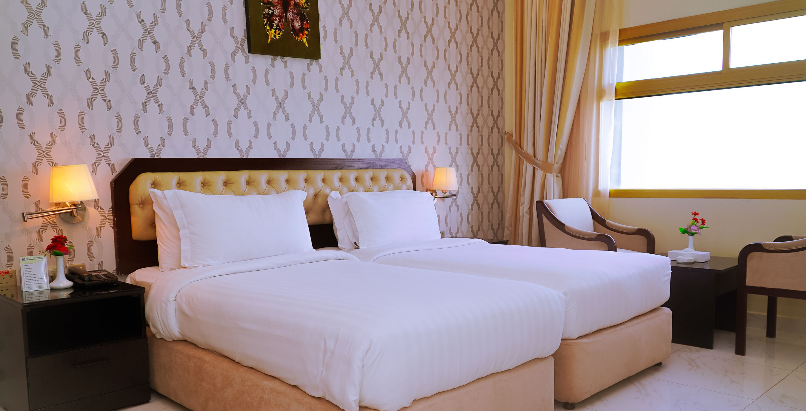 A hotel room with a double bed, two bedside tables, a chair, a desk, and a window with curtains.