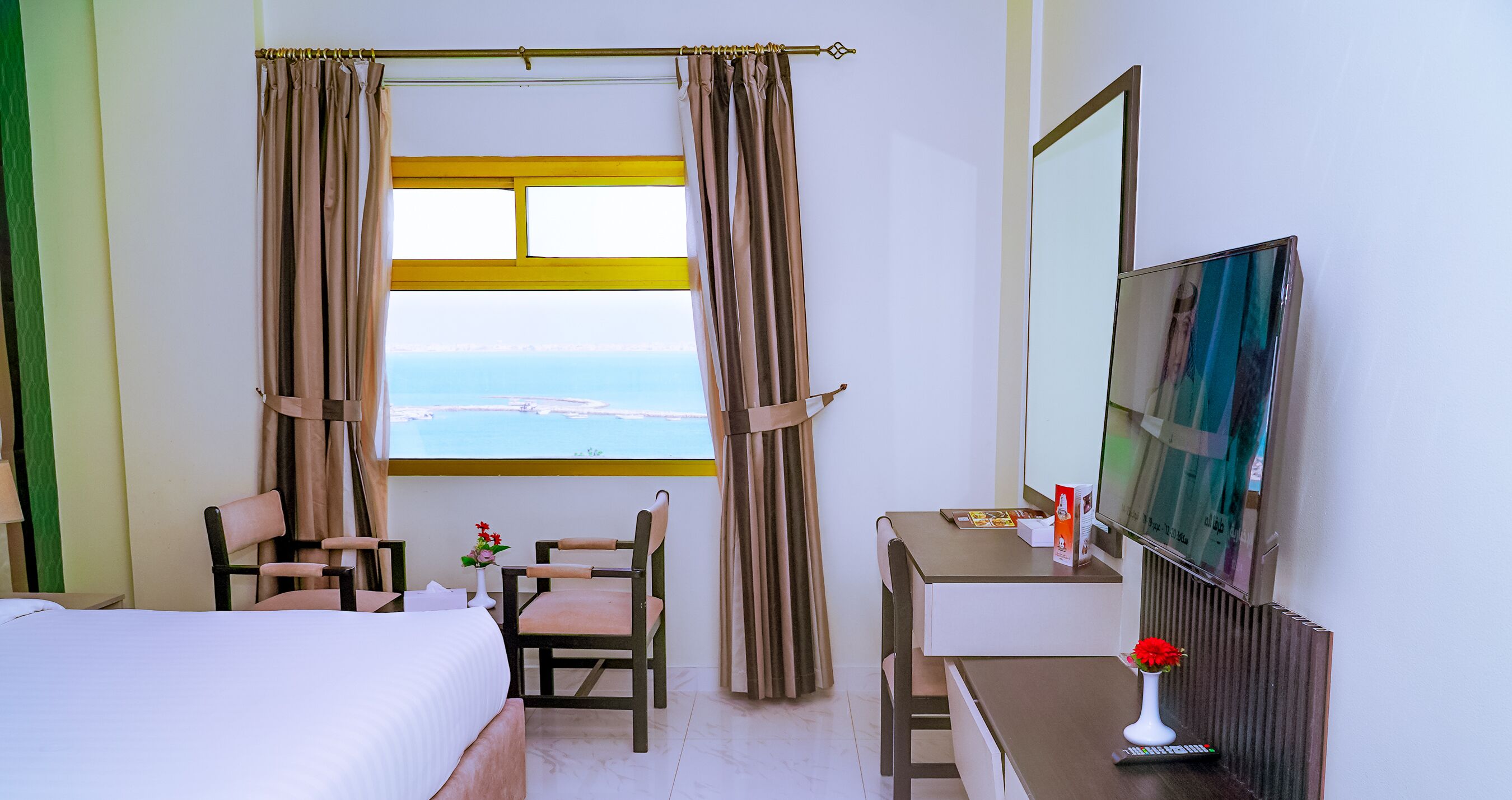 Habitación de hotel con cama, escritorio, silla, televisor y ventana con cortinas.