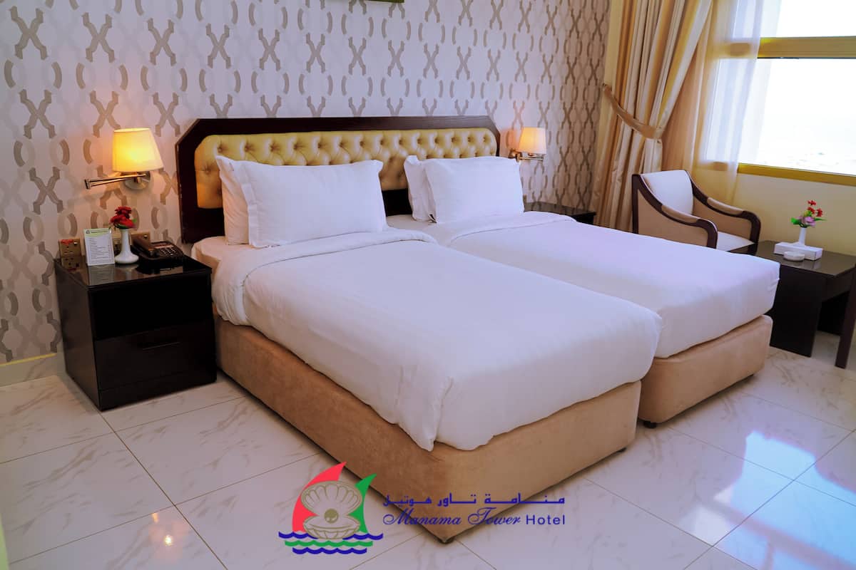 A hotel room with two beds, a nightstand with a lamp, a chair, and a small table with a vase of flowers.