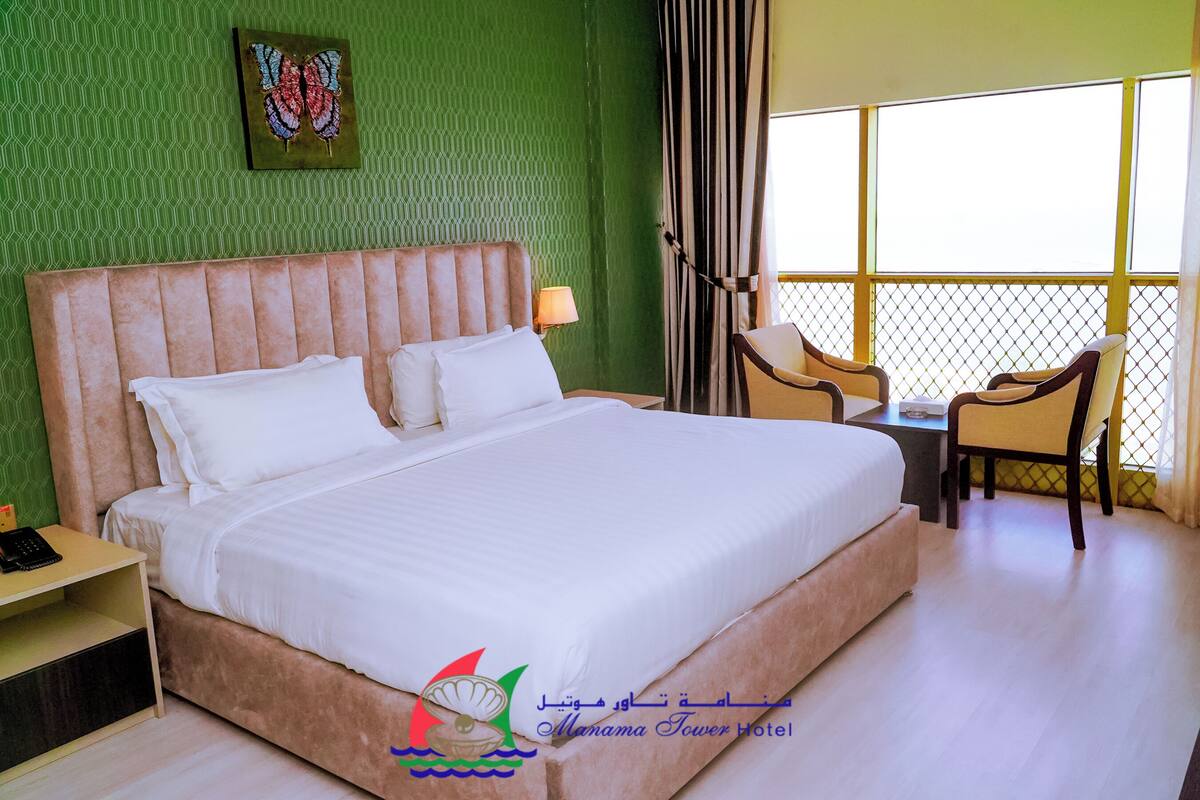 A hotel room with a large bed, a desk with a lamp, a chair, and a window with curtains.