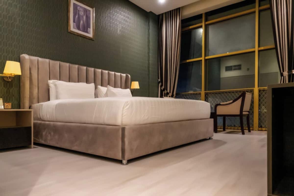 A neatly arranged bedroom with a large bed, bedside lamps, a chair, and a window with curtains.