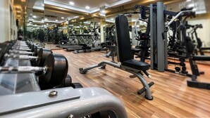 A gym with various exercise equipment, including dumbbells and weight machines, arranged on a wooden floor. - Capital O 126 Manama Tower Hotel (Manama)