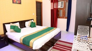 A hotel room with a bed, a nightstand, a chair, a window with curtains, and a door. - Hotel Abodes House (Noida)