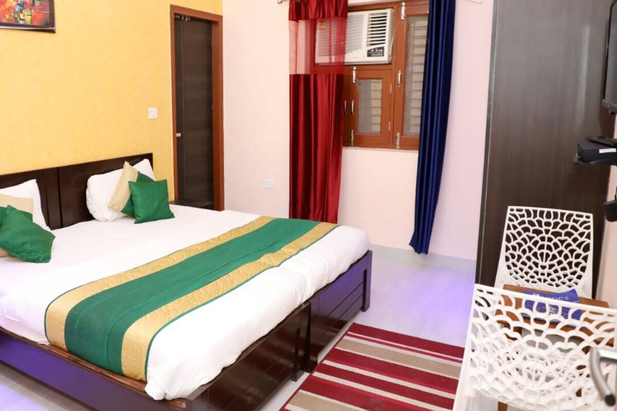 A hotel room with a bed, a nightstand, a chair, a window with curtains, and a door.