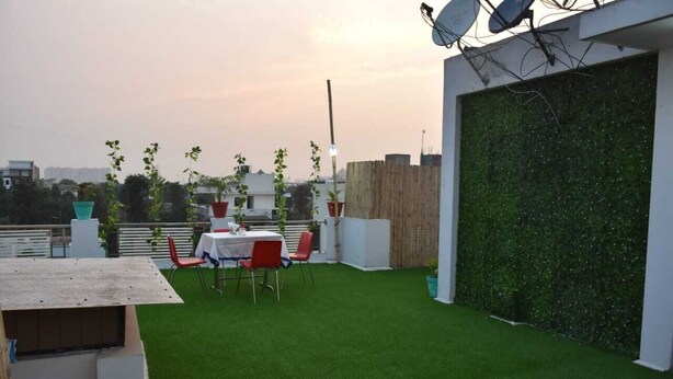 A rooftop terrace with artificial grass, a table with chairs, and potted plants. - Hotel Abodes House (Noida)