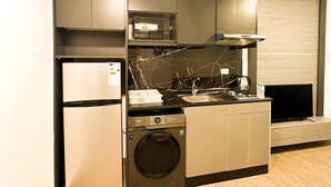 Uma cozinha compacta com micro-ondas, forno e máquina de lavar loiça embutidos, uma pia pequena e uma televisão de ecrã plano.