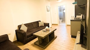 Sala de estar com sofá, mesa de centro, televisão e área de cozinha ao fundo.