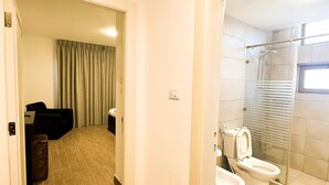 Casa de banho de hotel com chuveiro, sanita e área de duche com parede de vidro.