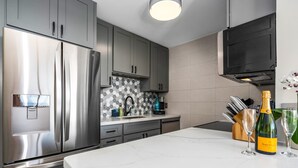 Une cuisine moderne dotée d’appareils électroménagers en acier inoxydable, de meubles gris, d’un plan de travail en marbre et d’une bouteille de vin.