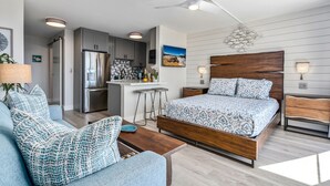 Une chambre moderne avec un lit en bois, une petite kitchenette et un coin salon comprenant un canapé et une table basse.