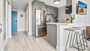 Une cuisine moderne avec des meubles gris, des appareils en acier inoxydable et un coin bar équipé de tabourets.