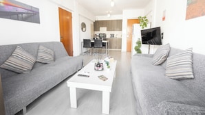 Ein modernes Wohnzimmer mit zwei grauen Sofas, einem weißen Couchtisch und einer Küche im Hintergrund.