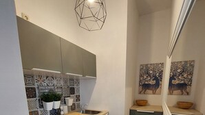 Une cuisine compacte au design moderne, dotée d’un luminaire suspendu aux formes géométriques, d’un four encastré et d’un petit évier.