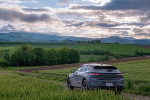 A car parked in a field with a mountainous landscape in the background. - Nozo Hotel (Furano)