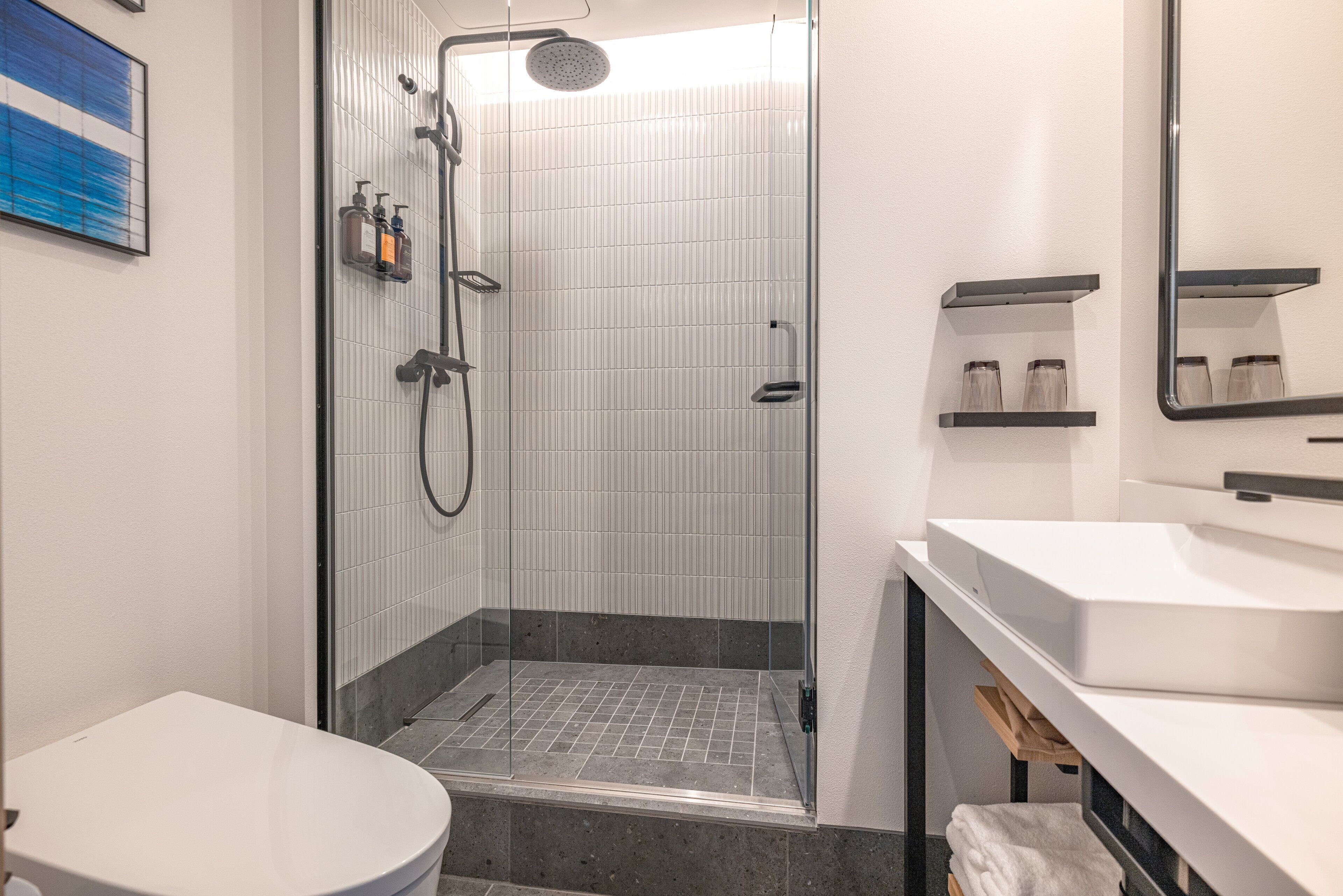 A modern bathroom with a glass-enclosed shower, a white toilet, and a vanity with a mirror and shelves.