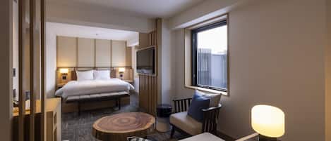 A modern hotel room with a large bed, a sofa, a coffee table, a TV, and a window with a view.