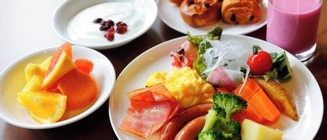 Un desayuno con platos de comida que incluyen frutas, verduras, huevos y salchichas.