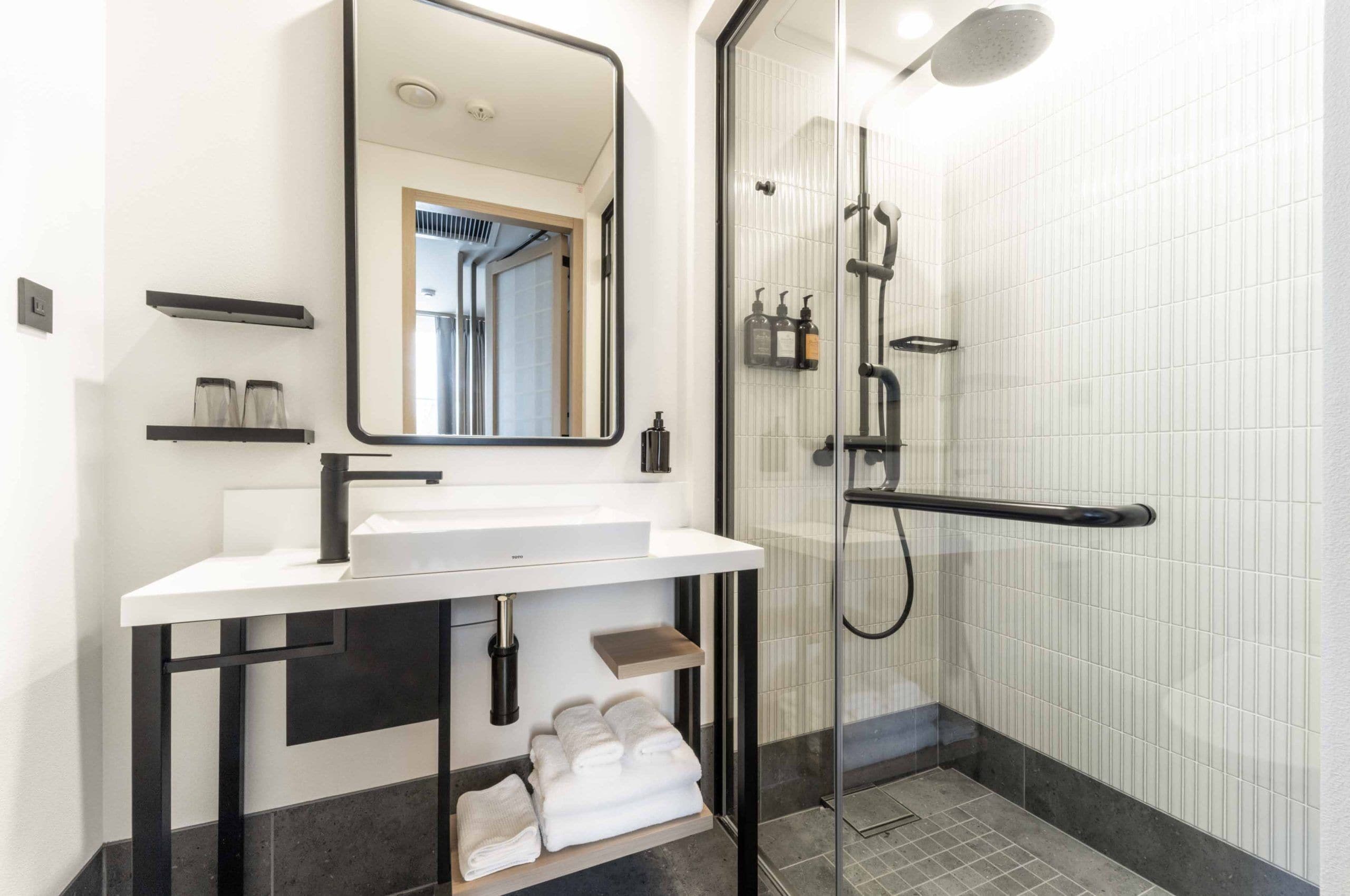 A modern bathroom with a white sink, black fixtures, a glass shower enclosure, and a mirror.