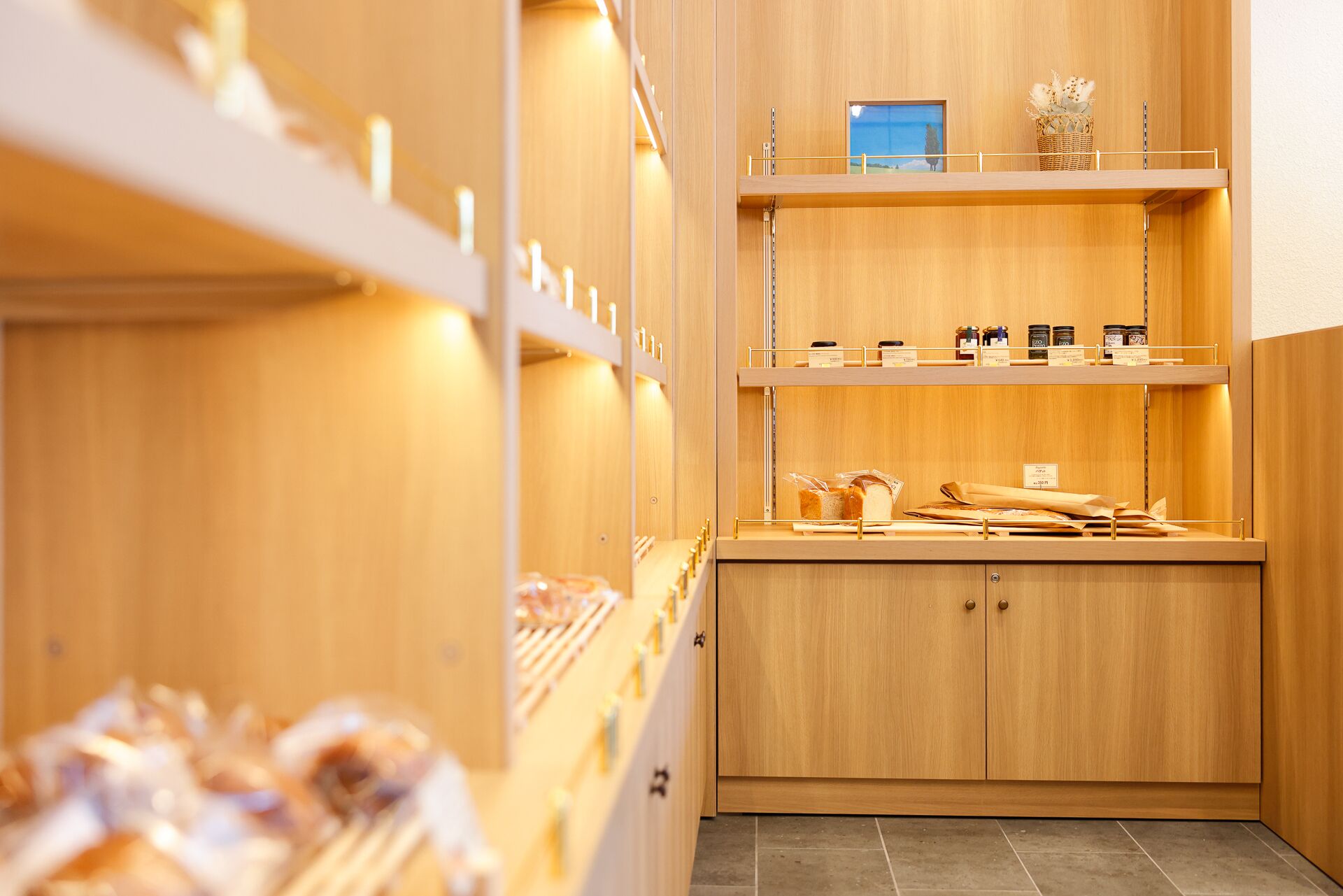 A bakery display with shelves of bread and pastries, wooden cabinets, and a tiled floor.