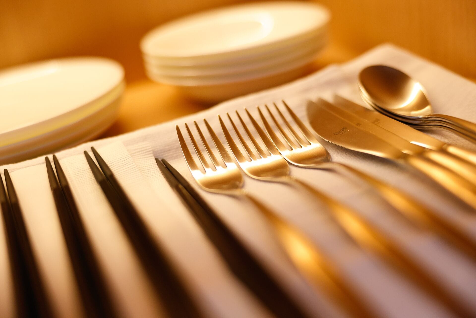 A close-up of a table setting with a white napkin, multiple forks, knives, and spoons.