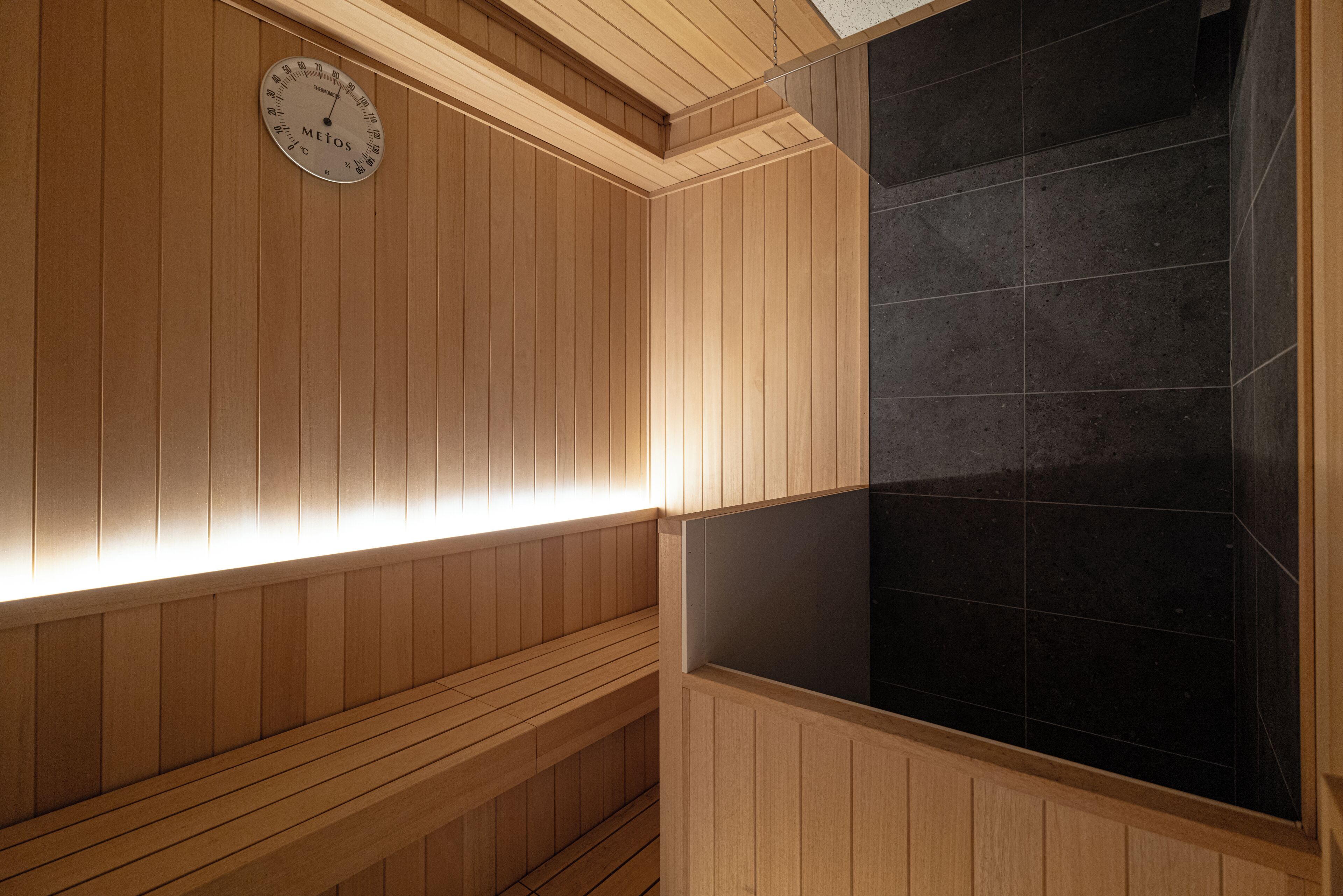 A wooden sauna with a clock on the wall, tiled walls, and benches.