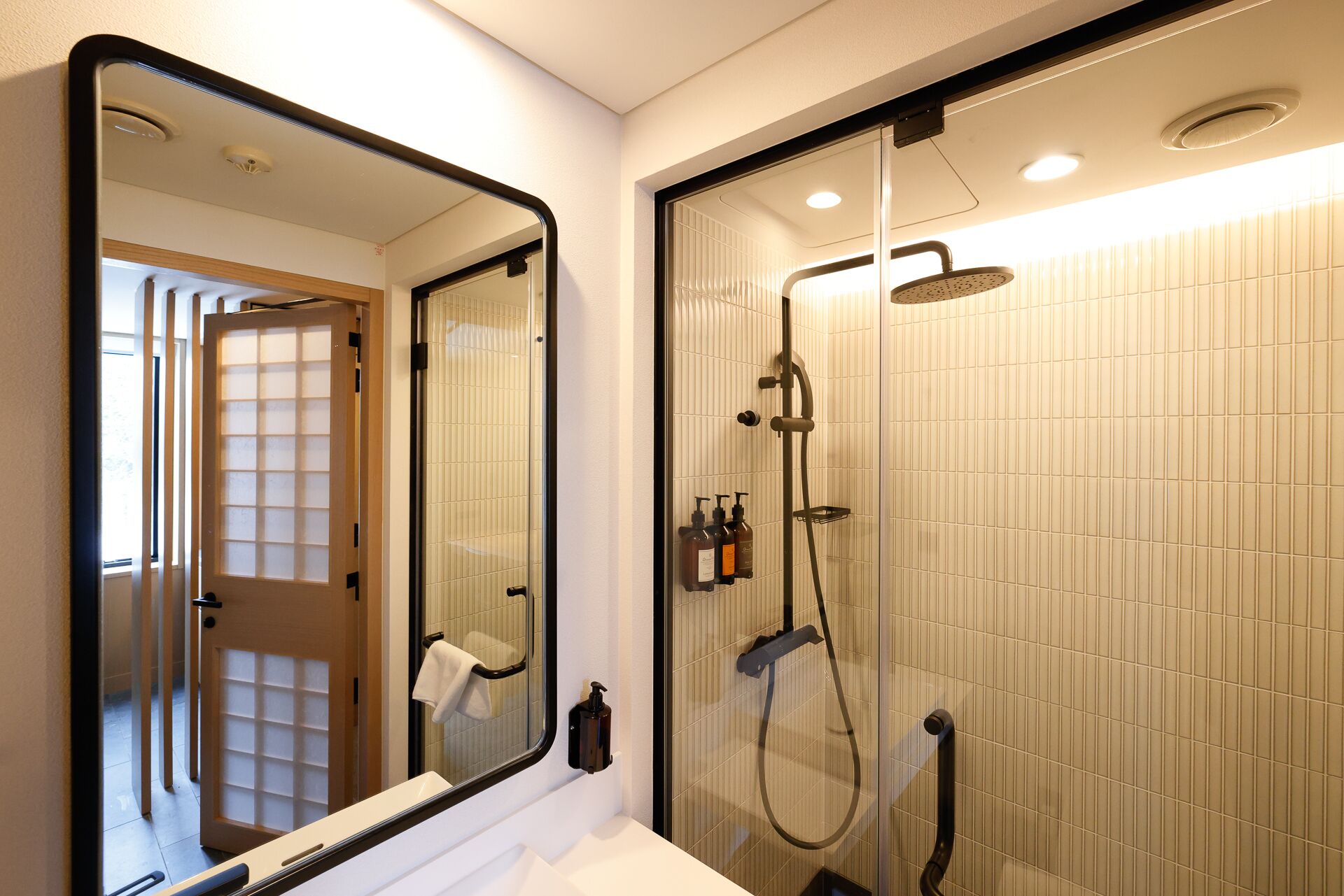 A bathroom with a large mirror, a glass-enclosed shower, and a white sink.