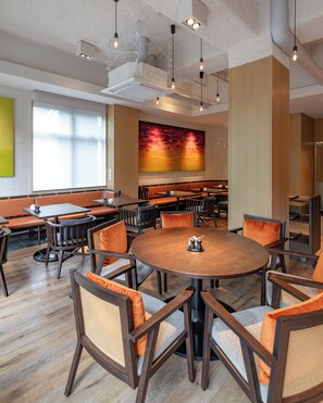A modern dining area with round tables and chairs, large windows, and a vibrant abstract painting on the wall. - Nozo Hotel (Furano)