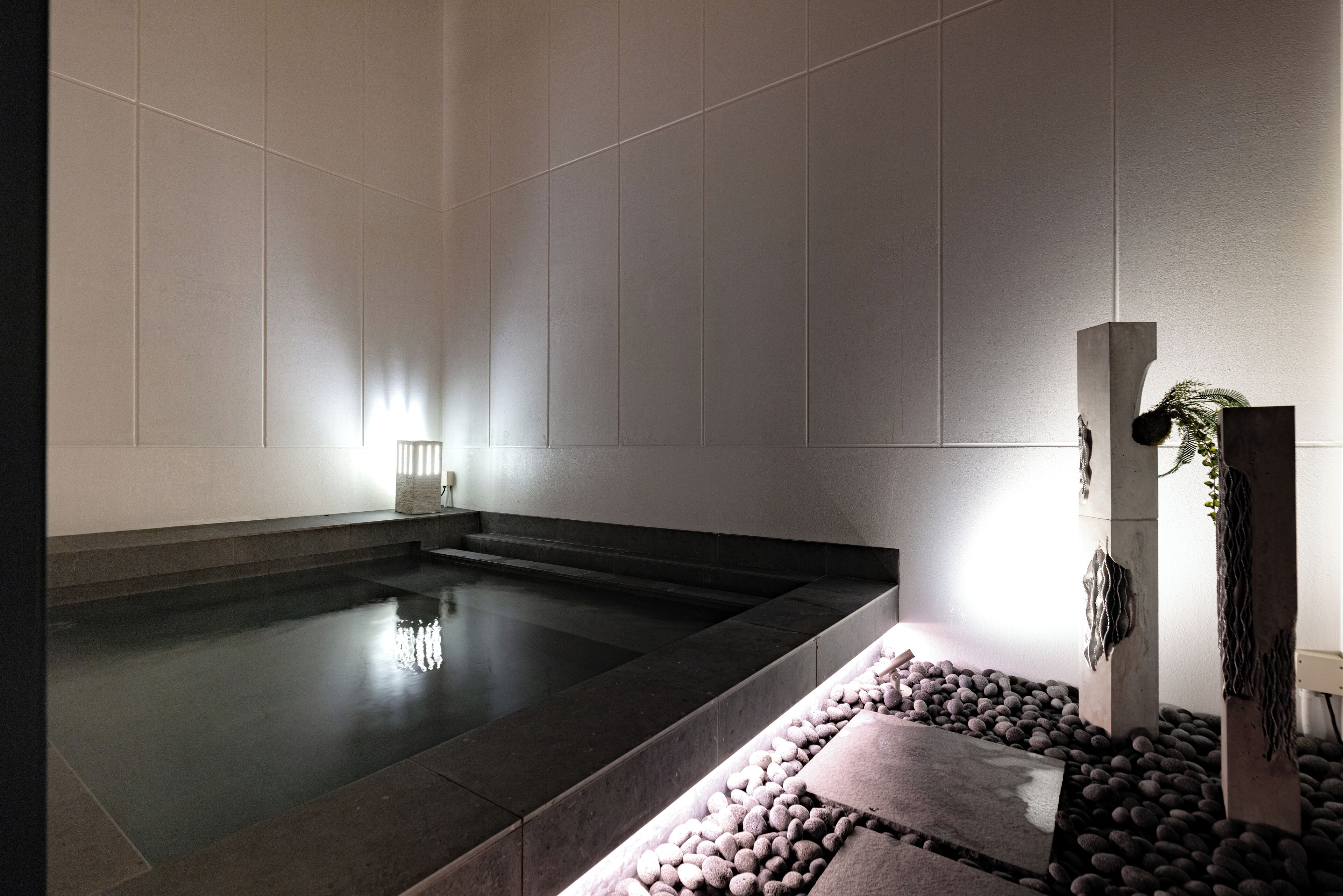 Un moderno espacio de spa con una amplia piscina oscura, asientos de piedra y una decoración minimalista.