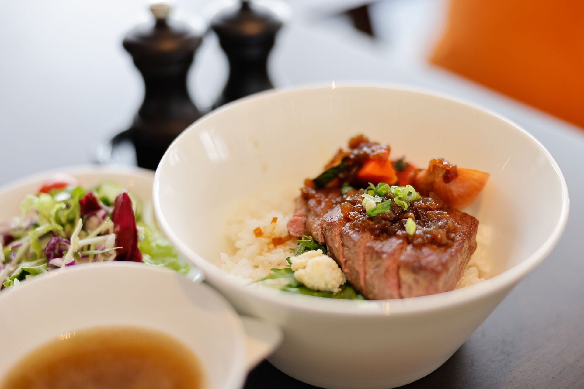 A bowl of food with a piece of meat, vegetables, and rice.